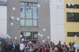 Schüler stehen vor einem Gebäude und lassen Luftballons steigen.