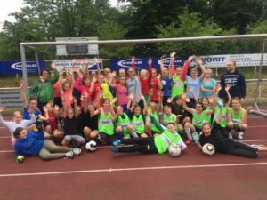 Gruppenshooting von Mädchenfußballspielern auf einem Sportplatz.