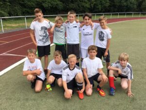 Gruppe von zehn Kindern in Sportkleidung auf einem Fußballplatz.