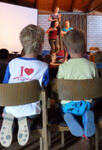 Zwei Kinder sitzen auf Stühlen und schauen einer Aufführung zu.