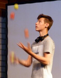 Junge jongliert mit bunten Bällen auf der Bühne.