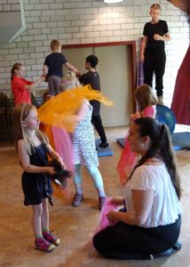 Kinder und Erwachsene spielen mit bunten Tüchern in einem Raum.