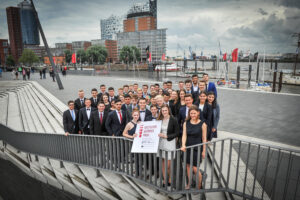 Gruppenfoto von 40 Personen vor einer modernen Stadtlandschaft am Wasser.