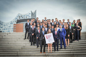 Gruppenfoto von mehreren Personen in Anzügen vor einem modernen Gebäude.