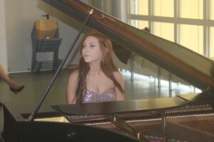 Eine junge Frau spielt Klavier in einem hellen Raum.