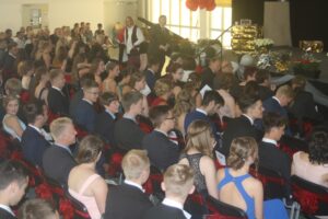 Schülerinnen und Schüler sitzen in eleganter Kleidung bei einer Veranstaltung.