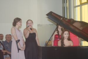Zwei Sängerinnen treten auf, während eine Pianistin am Klavier spielt.