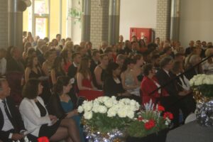 Schüler und Gäste sitzen bei einer festlichen Veranstaltung in einem Saal.