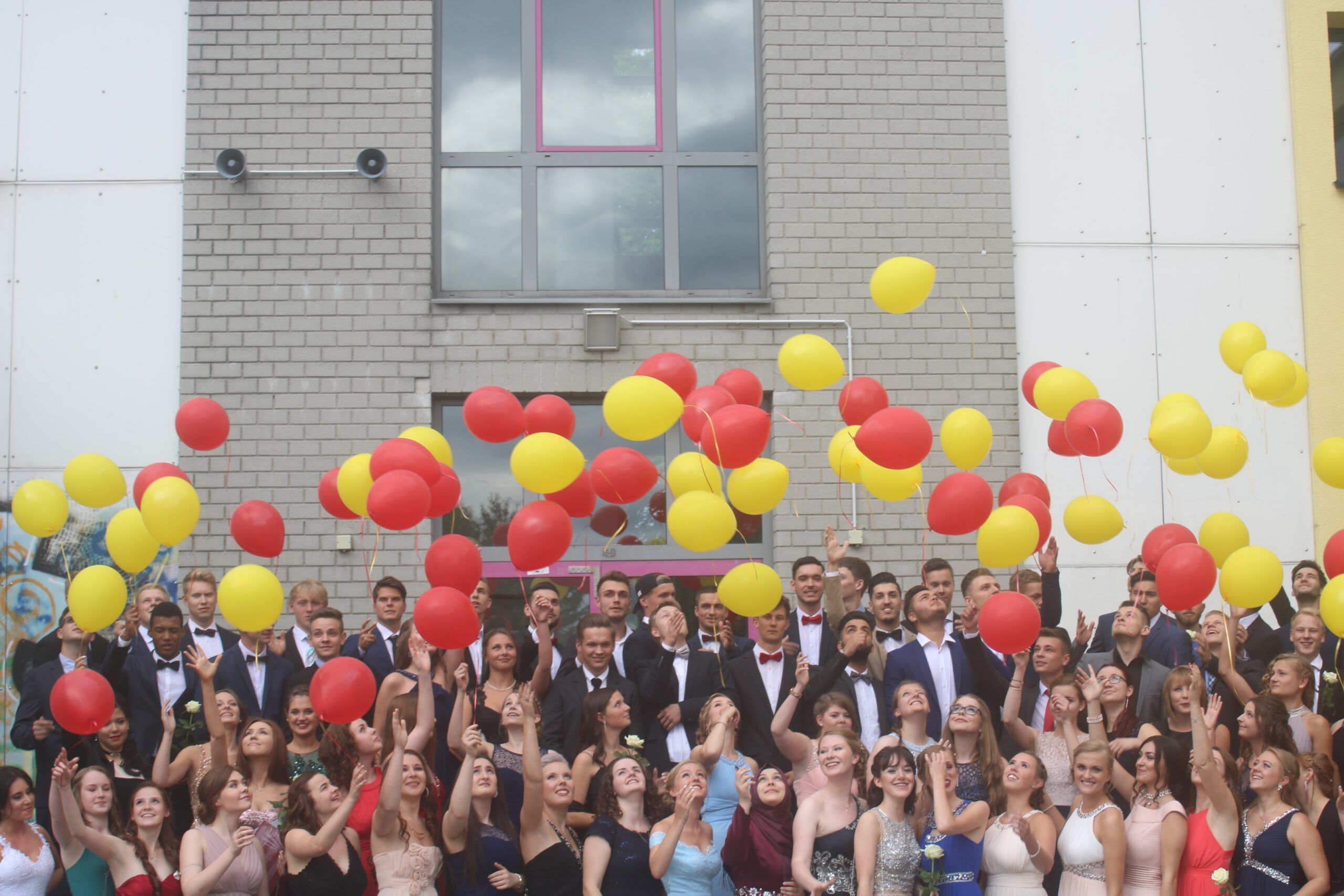 Gruppennfoto von Schülern mit roten und gelben Luftballons vor einem Gebäude.