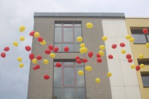 Bunte Luftballons in Rot und Gelb schweben vor einem Gebäude.
