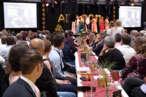 Veranstaltung mit Publikum, festlich dekorierten Tischen und einer Bühnenshow.