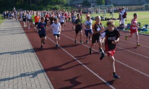 Schüler laufen auf einer Laufbahn bei einem Wettlauf. Zuschauer schauen zu.