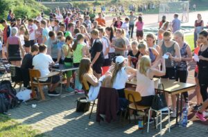 Schülerinnen und Schüler stehen an mehreren Tischen im Freien und warten.