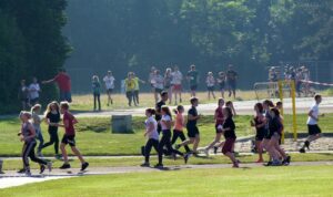 Schüler laufen auf einem Sportplatz, Zuschauer stehen im Hintergrund.