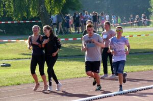 Schüler joggen auf der Laufbahn, Zuschauer stehen im Hintergrund.