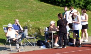 Gruppe von Personen auf einer Sportanlage, einige sitzen, andere stehen zusammen.