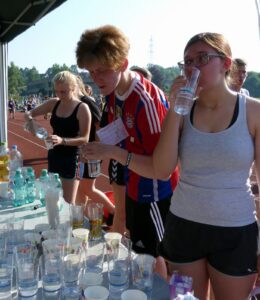Schüler füllen Gläser mit Wasser an einem Tisch bei einem Sportereignis.