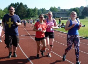 Vier Personen joggen auf einer Tartanbahn bei sonnigem Wetter.