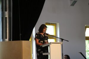 Frau spricht am Rednerpult in einem hellen Innenraum.