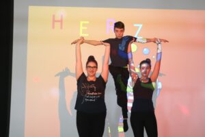 Drei Personen posieren vor buntem Hintergrund mit Lichtprojektionen.