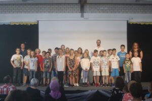 Gruppenszene von Schülern und Lehrern auf einer Bühne während einer Veranstaltung.