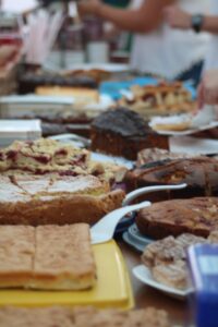 Tisch mit verschiedenen Kuchen und Süßspeisen in einer geschäftigen Umgebung.