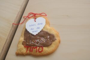 Herzförmiger Keks mit Schokolade und einer Grußkarte.