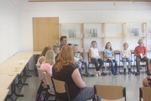 Gruppe von Kindern und Erwachsenen in einem Klassenraum bei einer Sitzung.