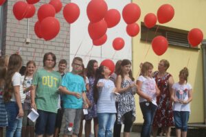 Schülerinnen und Schüler halten rote Ballons und stehen in Gruppen.
