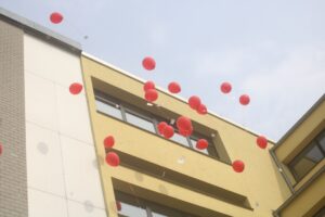 Rote Luftballons schweben vor einem gelben Gebäude.