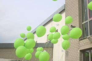 Grüne Luftballons schweben vor einem Gebäudewand.