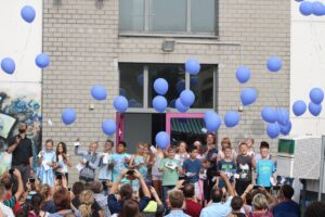 Schülerinnen und Schüler stehen vor einem Gebäude und lassen blaue Ballons steigen.