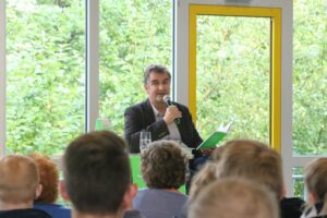 Mann spricht in einem Raum vor Publikum, Fenster mit Blick ins Grüne.