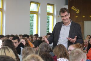 Lehrer spricht vor einer Gruppe von Schülern in einem Klassenraum.