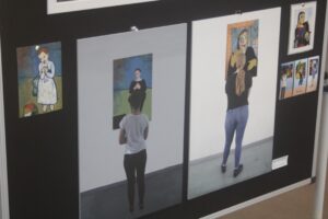 Ausstellung mit Bildern an Wänden und Personen, die sie betrachten.