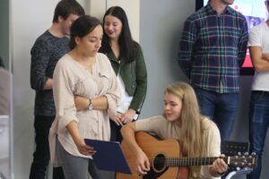Schülerin spielt Gitarre, andere hören zu und schauen gespannt.