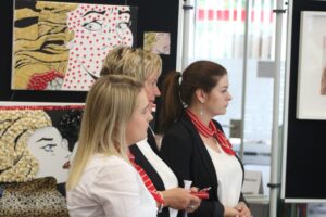 Drei Frauen stehen vor einer Kunst-Ausstellung mit Bildern im Hintergrund.