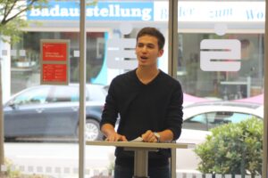 Junger Mann spricht an einem Rednerpult vor einer Glasfront.