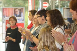 Gruppe von Menschen applaudiert in einem hellen Raum.