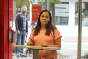 Frau mit pinkem Shirt steht an einem Stehtisch, im Hintergrund eine Person.