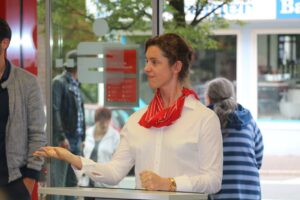 Frau mit rotem Schal steht an einem Empfangstresen.