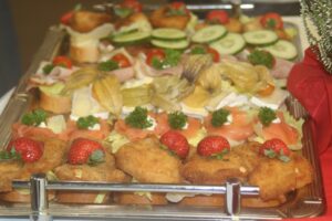 Bunte Platten mit belegten Brötchen, Fisch, Obst und Gemüse.
