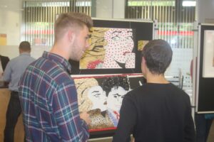 Zwei Schüler betrachten Kunstwerke auf einer Ausstellungstafel.