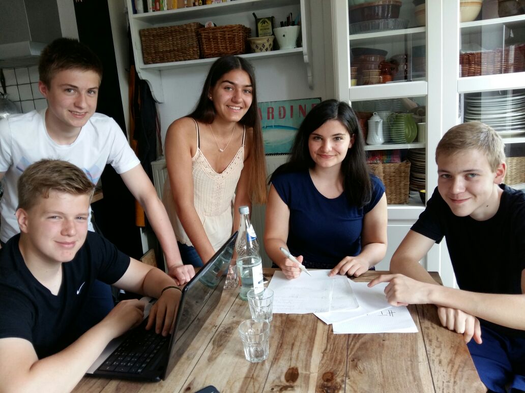 Schüler arbeiten am Tisch an einem Projekt mit Laptop und Unterlagen.