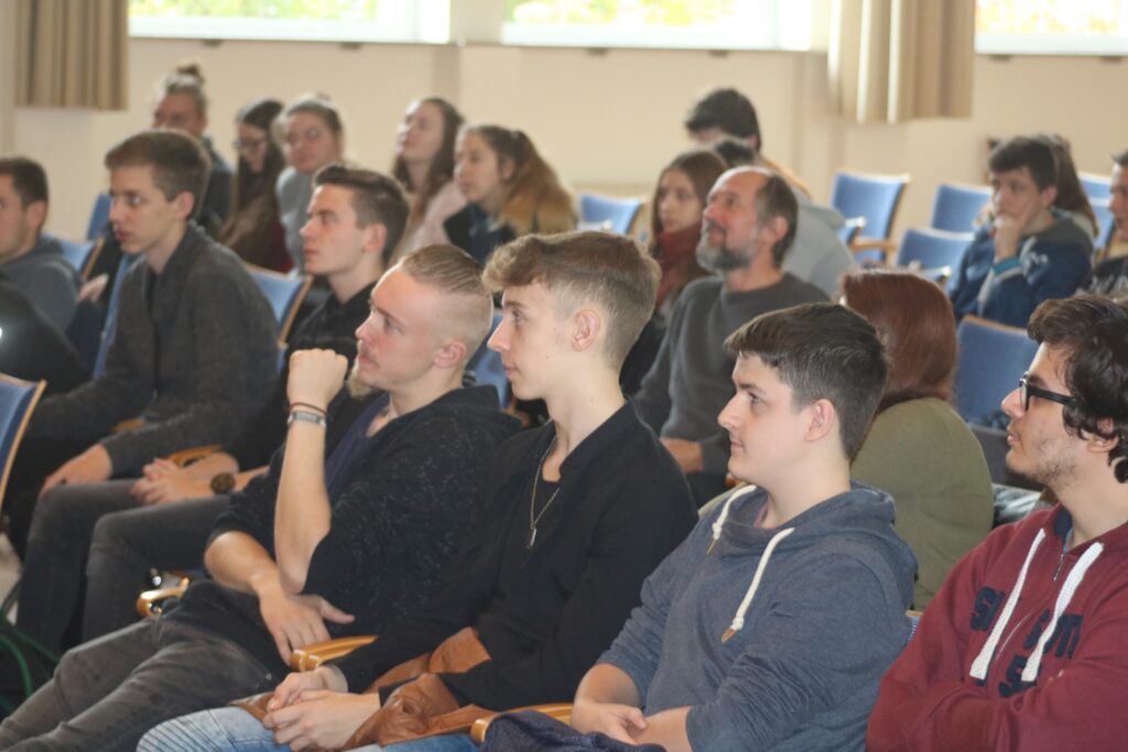 Gruppe von Personen sitzt in einem Raum und hört einer Präsentation zu.