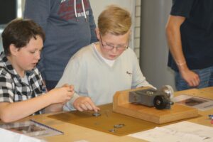 Zwei Schüler arbeiten an einem technischen Projekt mit Maschinen und Werkzeugen.