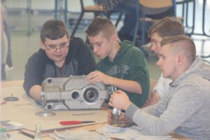 Schüler arbeiten gemeinsam an einem Motorblock in einem Klassenzimmer.