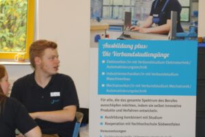 Junger Mann sitzt vor einem Informationsbanner zu Ausbildungsplätzen.
