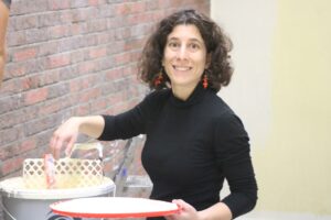 Eine Frau mit lockigem Haar lächelt und hält eine rote Schüssel.