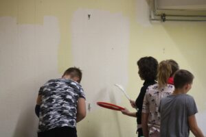 Schüler streichen eine Wand in einem Klassenraum.